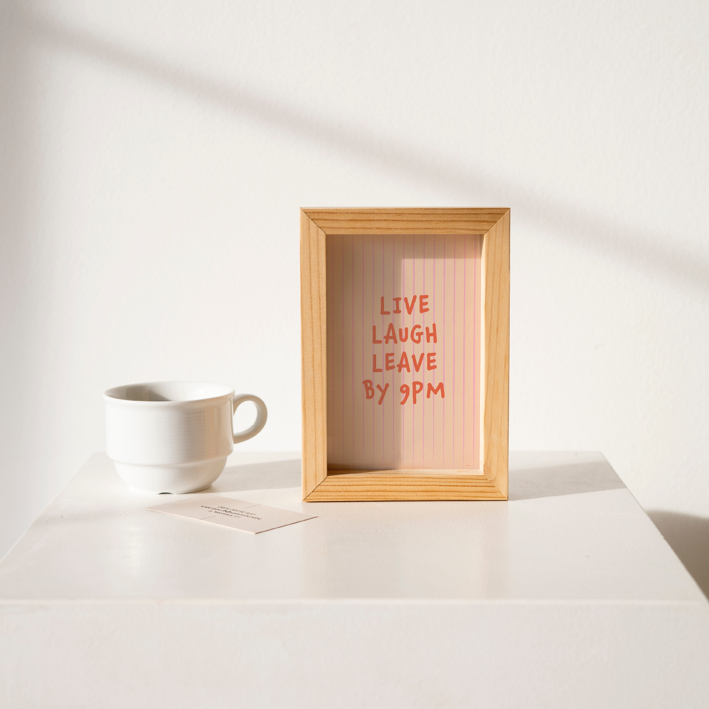 Small "Live, Laugh, Leave by 9 PM" Wall Art Print in pink. Framed cute wall decor / entryway artwork on a clean white table.
