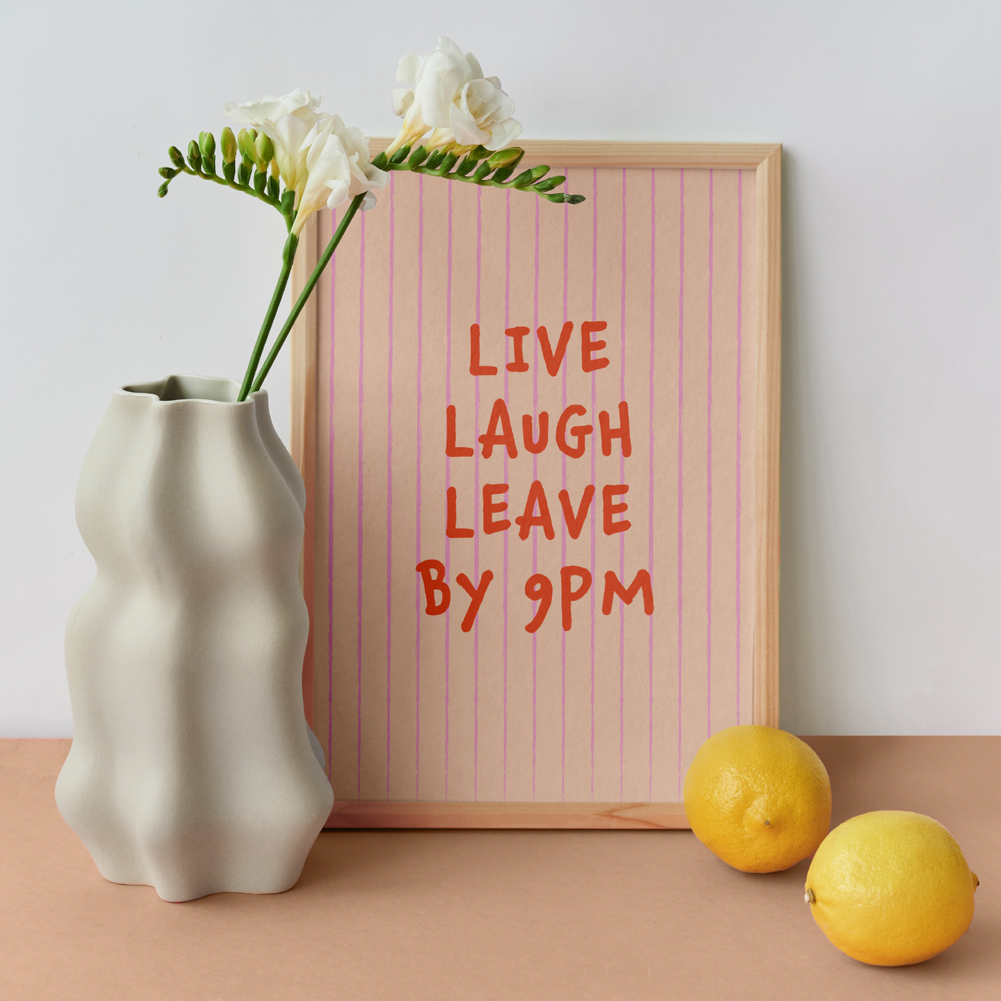 Medium "Live, Laugh, Leave by 9 PM" Wall Art Print in pink. Framed cute wall decor / entryway artwork next to a white vase.