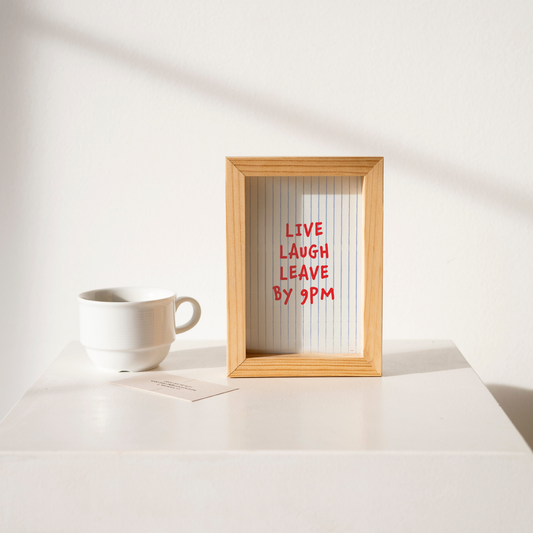 Small "Live, Laugh, Leave by 9 PM" Wall Art Print in blue with red words. Framed cute wall decor / entryway artwork on a clean white table.