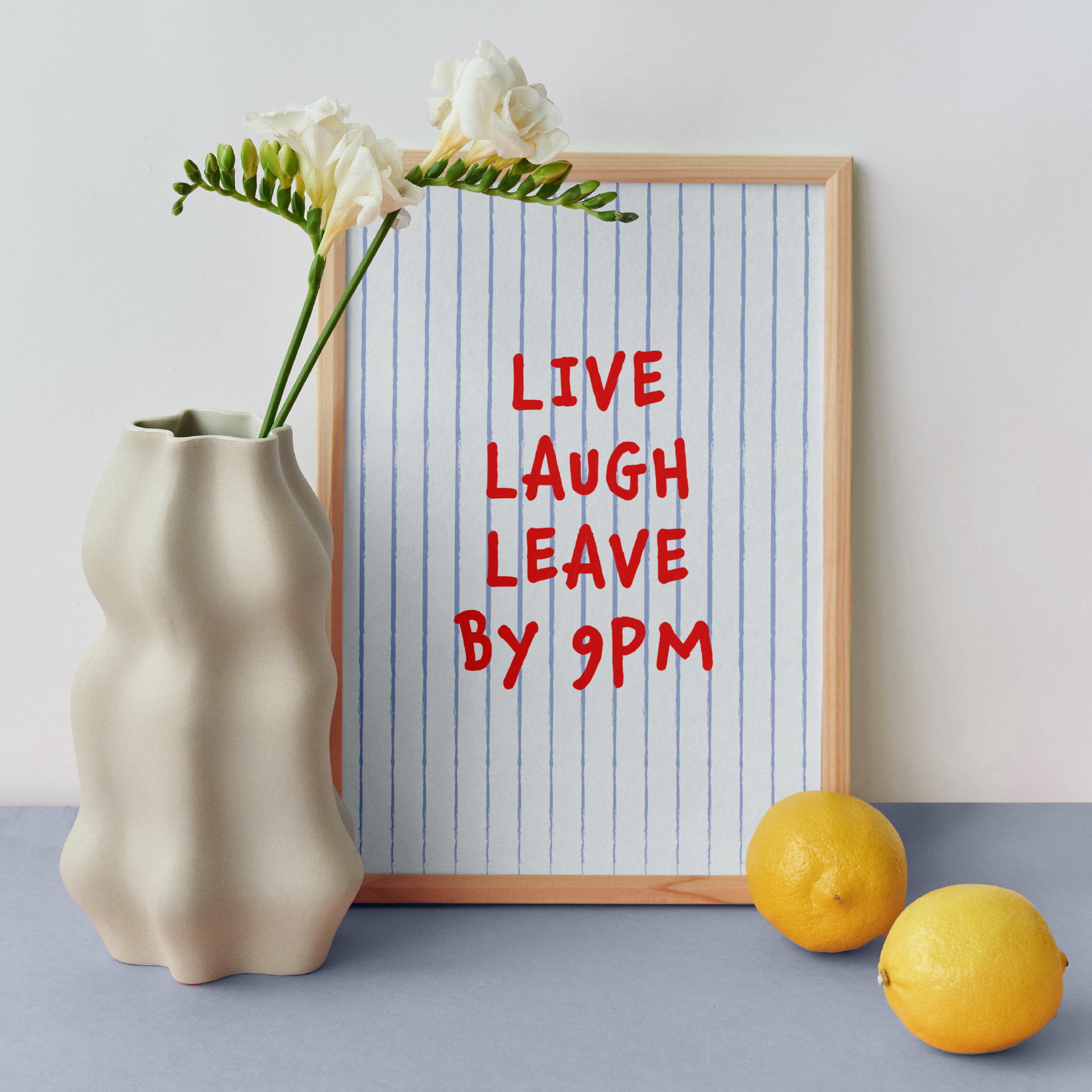 Medium "Live, Laugh, Leave by 9 PM" Wall Art Print in light blue with red words. Framed cute wall decor / entryway artwork next to a white vase.