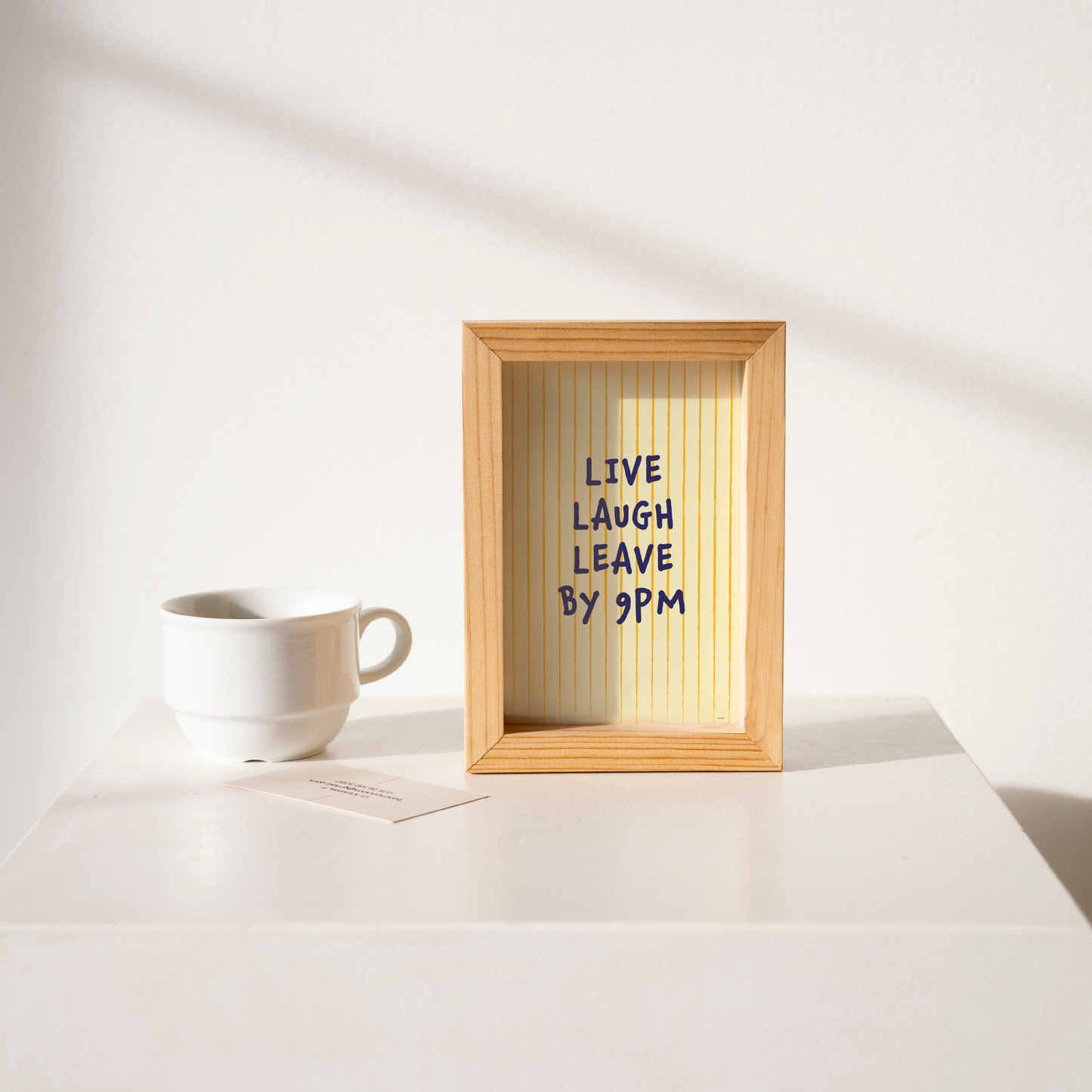 Small "Live, Laugh, Leave by 9 PM" Wall Art Print in yellow. Framed cute wall decor / entryway artwork on a clean white table.
