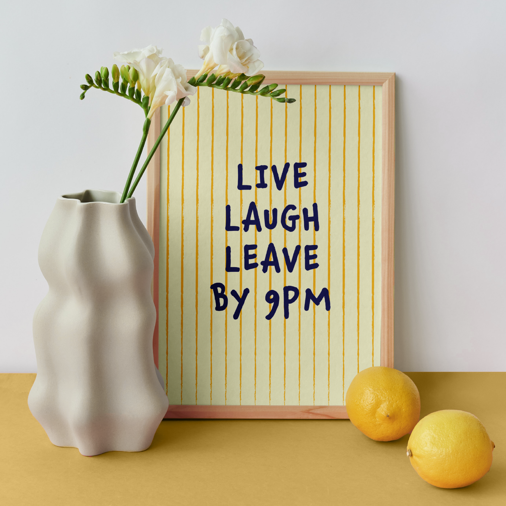 Medium "Live, Laugh, Leave by 9 PM" Wall Art Print in yellow. Framed cute wall decor / entryway artwork next to a white vase.