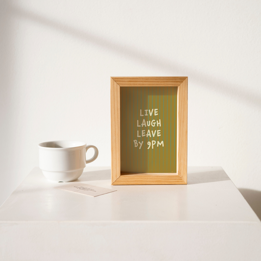 Small "Live, Laugh, Leave by 9 PM" Wall Art Print in green. Framed cute wall decor / entryway artwork on a clean white table.