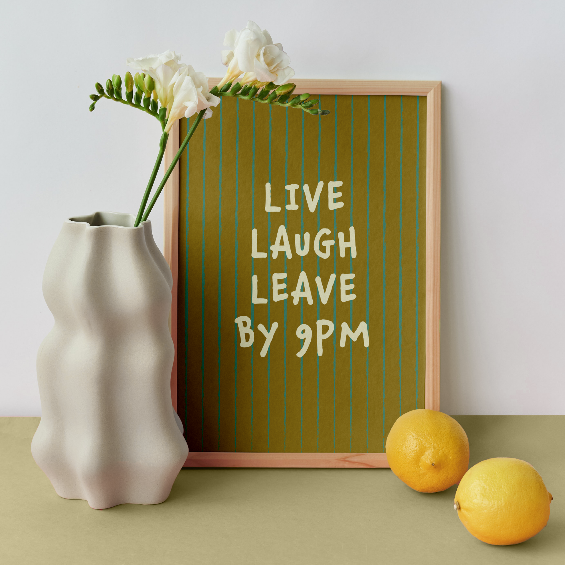 Medium "Live, Laugh, Leave by 9 PM" Wall Art Print in green. Framed cute wall decor / entryway artwork next to a white vase.