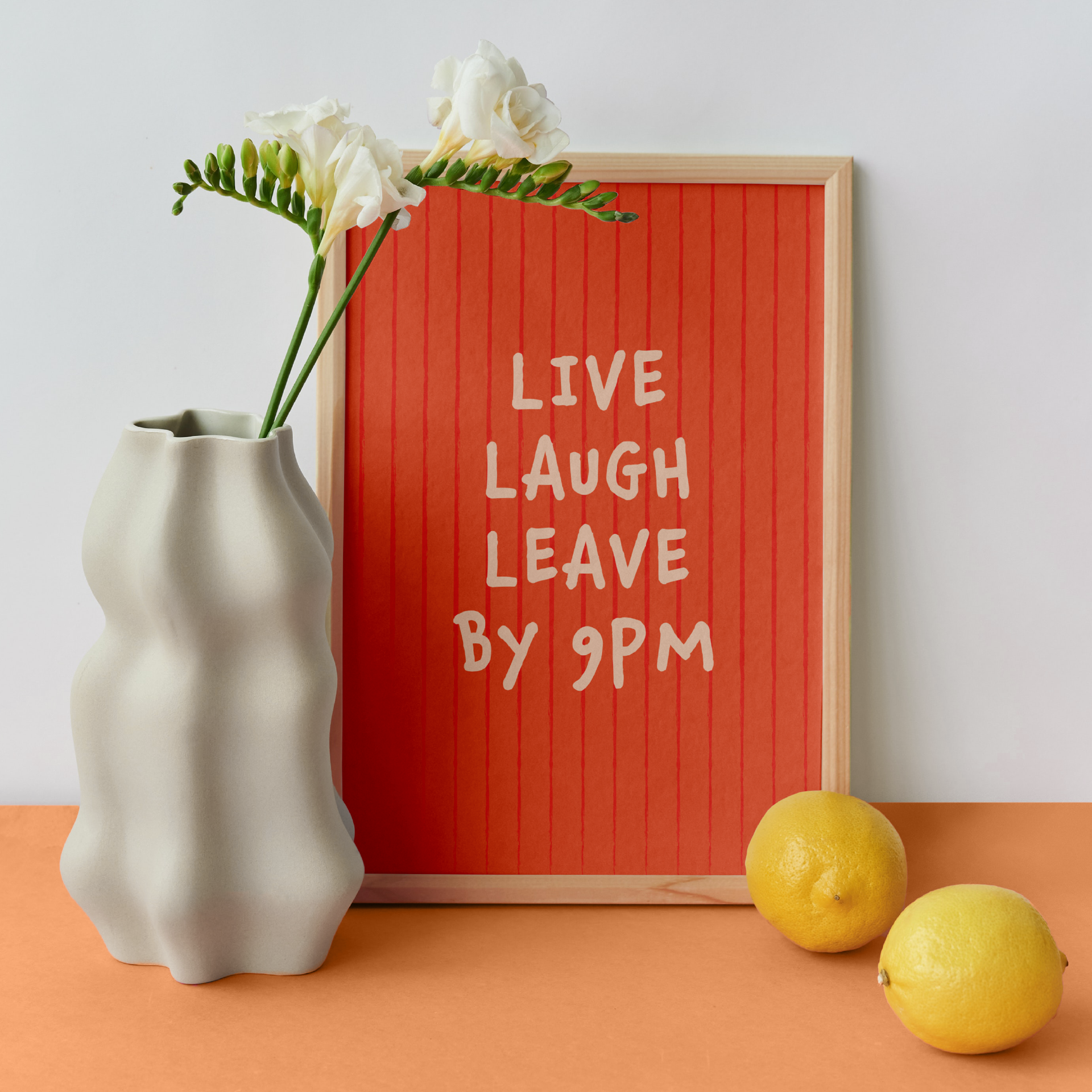 Medium "Live, Laugh, Leave by 9 PM" Wall Art Print in coral. Framed cute wall decor / entryway artwork next to a white vase.