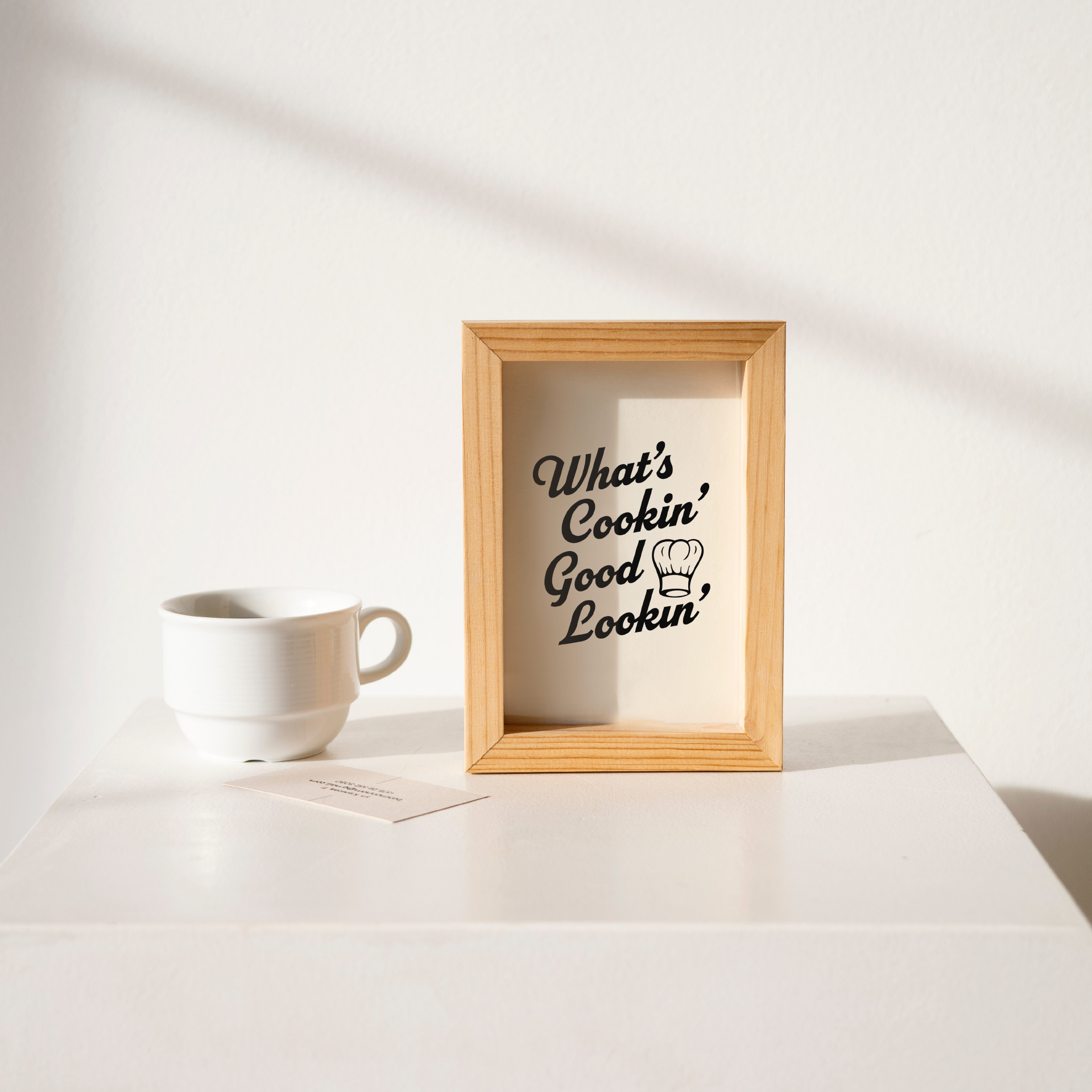 Small "What's Cookin' Good Lookin'" Kitchen Wall Art Print in black on warm off-white. Framed cute wall decor on a clean white table.
